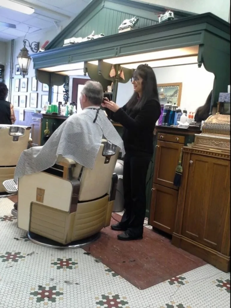 Lisa cutting a customer's hair at the green back bar, over the mosaic tile floor