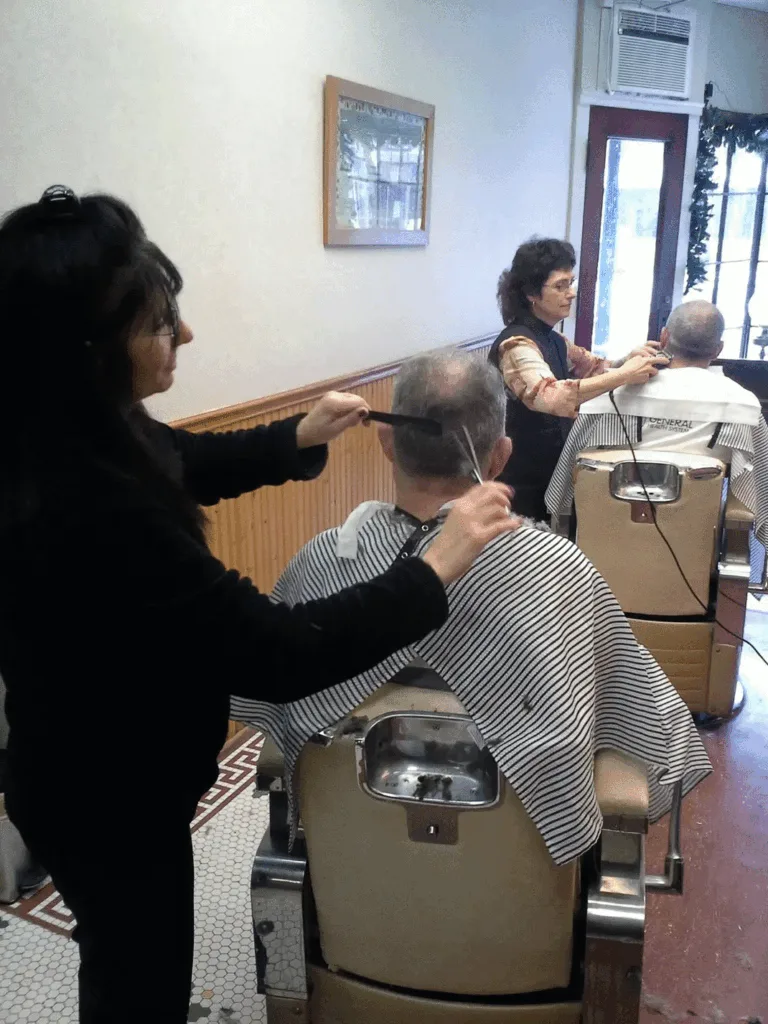 Lisa and a second barber cutting two customers' hair side by side