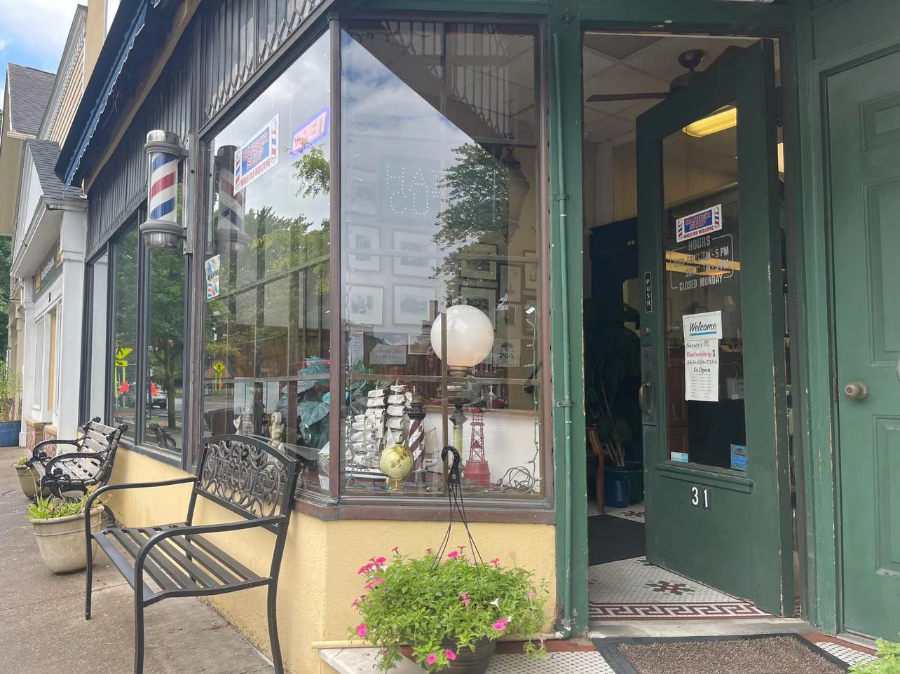 The shop's front window and open green door at number 31, with a barber pole and a bench on the sidewalk